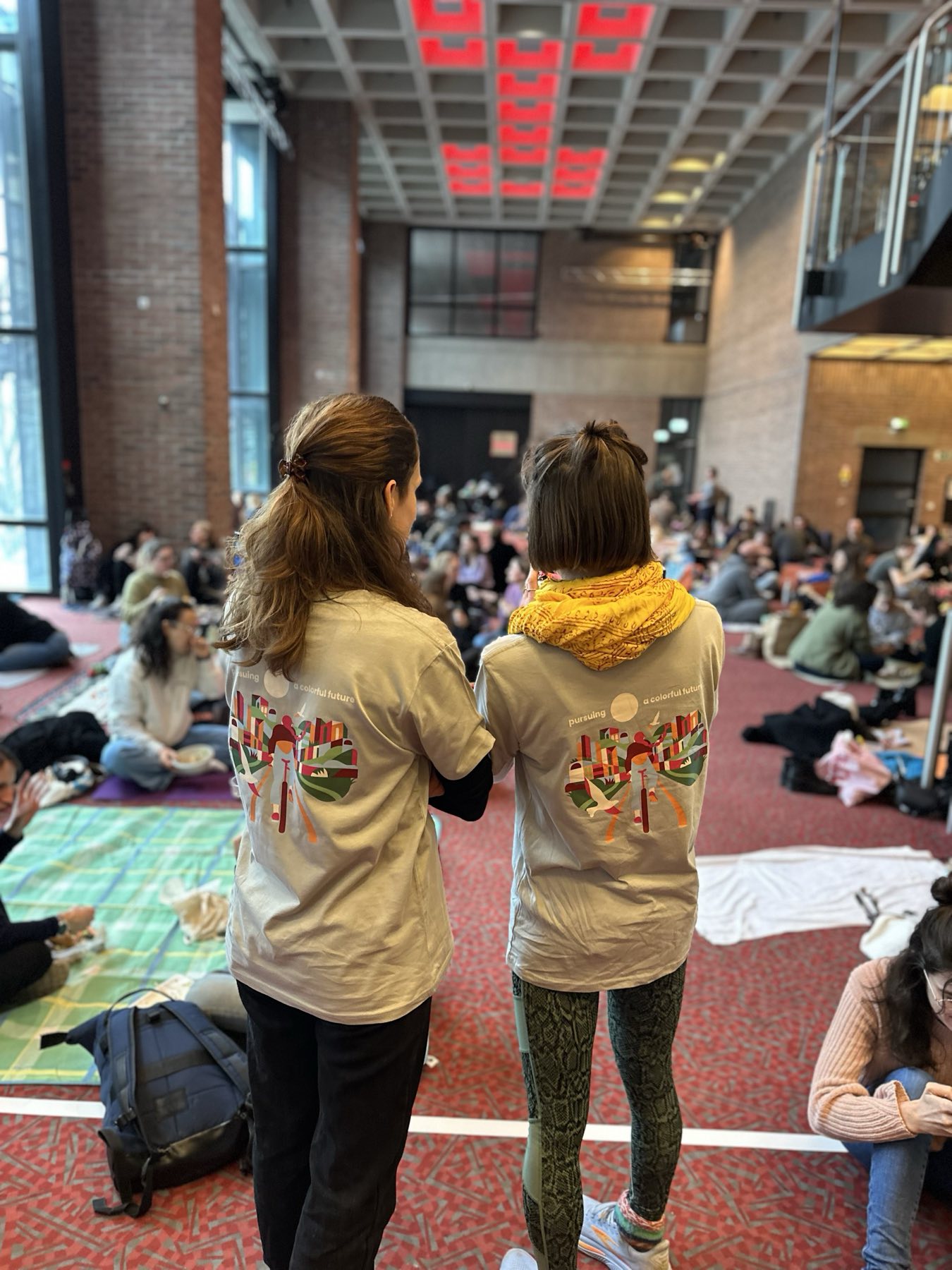 Zwei Gäste in Event-Shirts von hinten, Blick in die volle Halle